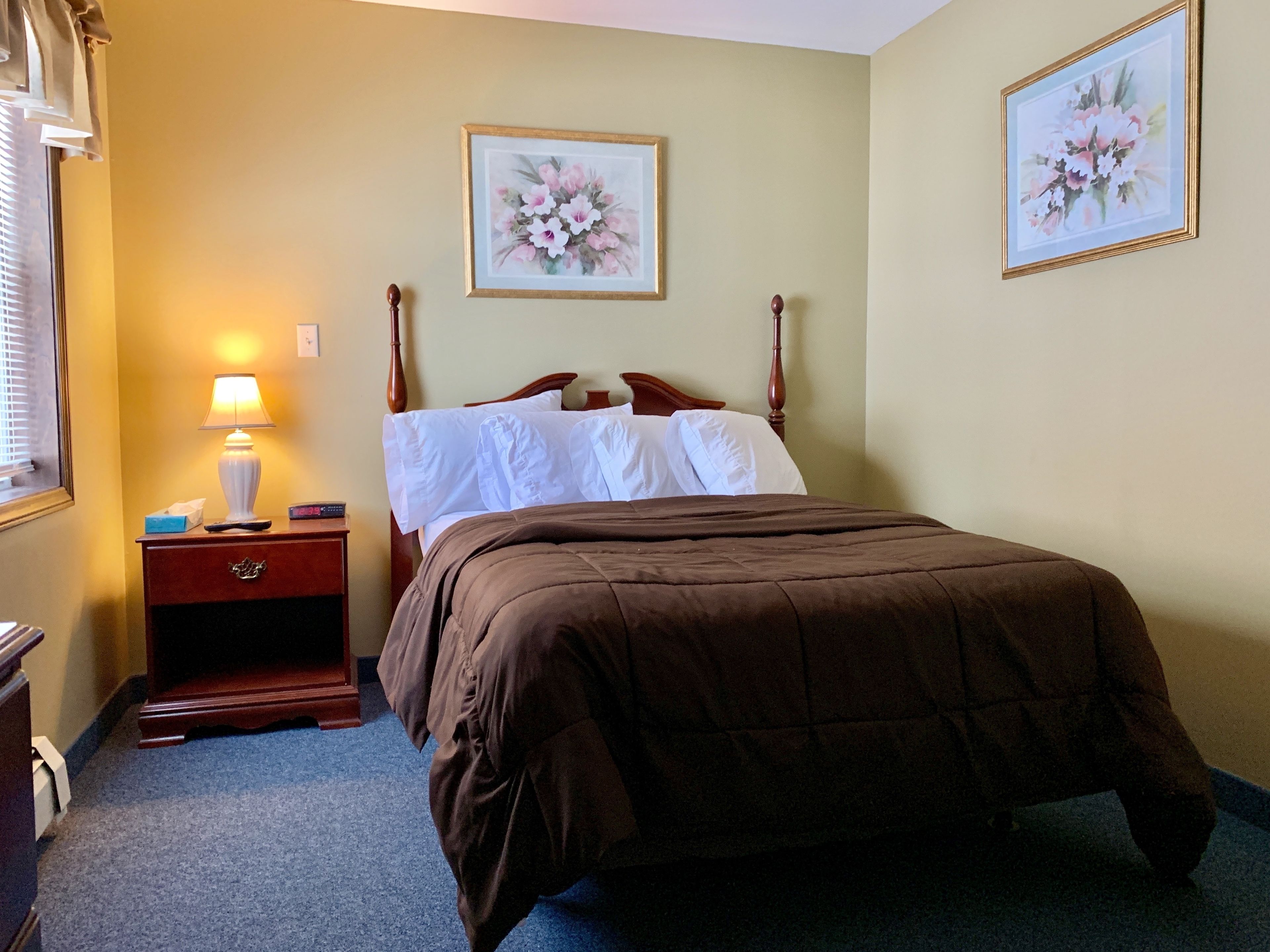 Ein Hotelzimmer mit einem Bett, einem Nachttisch mit Lampe und zwei gerahmten floralen Bildern an der Wand.