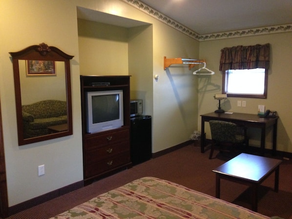 Una habitación de hotel con cama, escritorio, silla, televisor y espejo.
