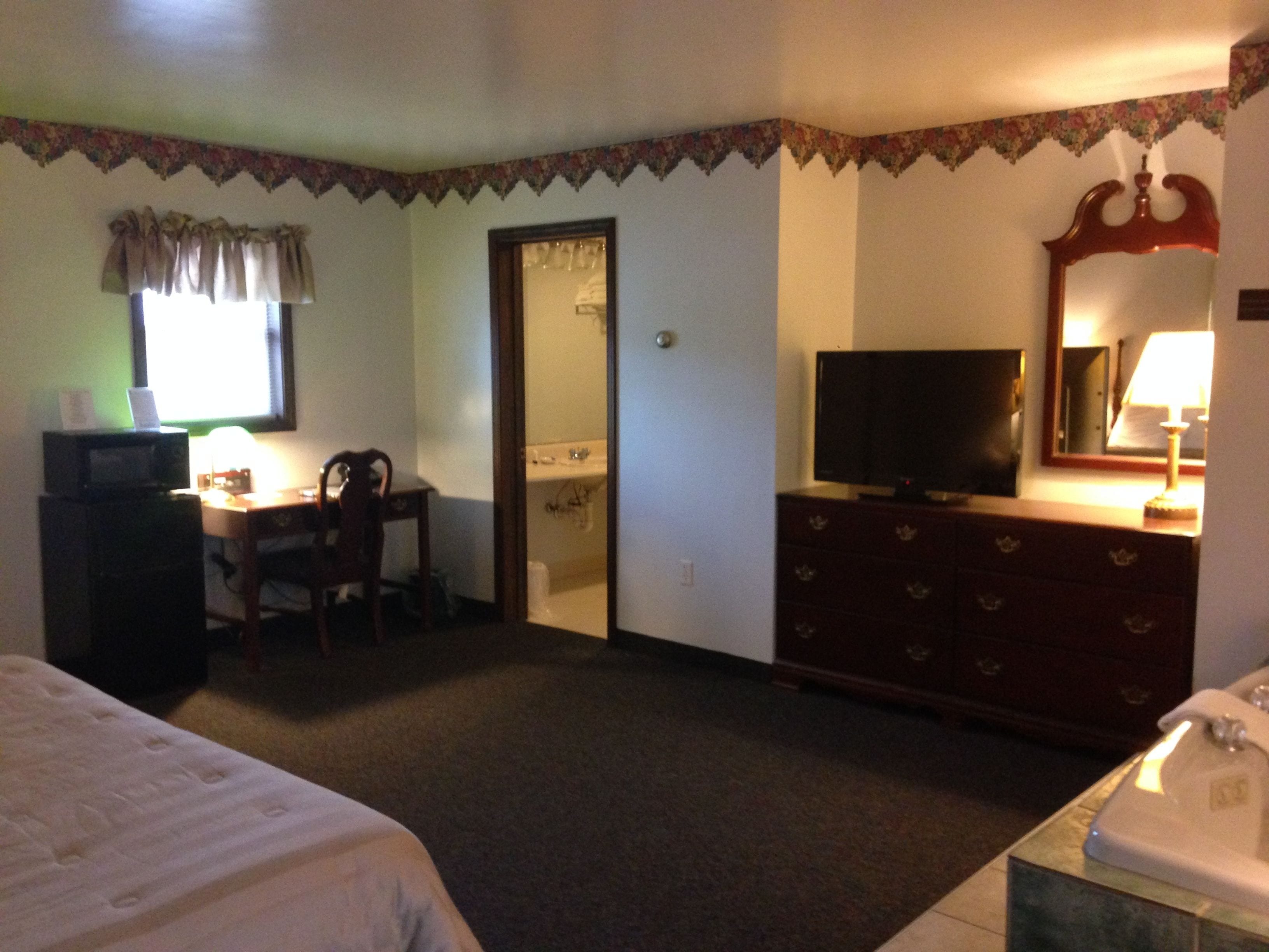 Habitación de hotel con cama, escritorio con computadora, televisión, cómoda y baño.