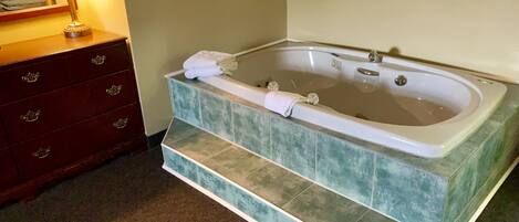 A bathroom with a large bathtub, a wooden vanity with drawers, and a lamp.