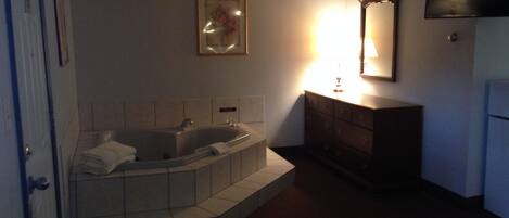 Ein Badezimmer mit einer Badewanne, einem Waschtisch inklusive Spiegel und einem an der Wand montierten Fernseher.