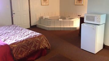 A hotel room with a bed, a bathroom with a bathtub, a microwave, and a television.