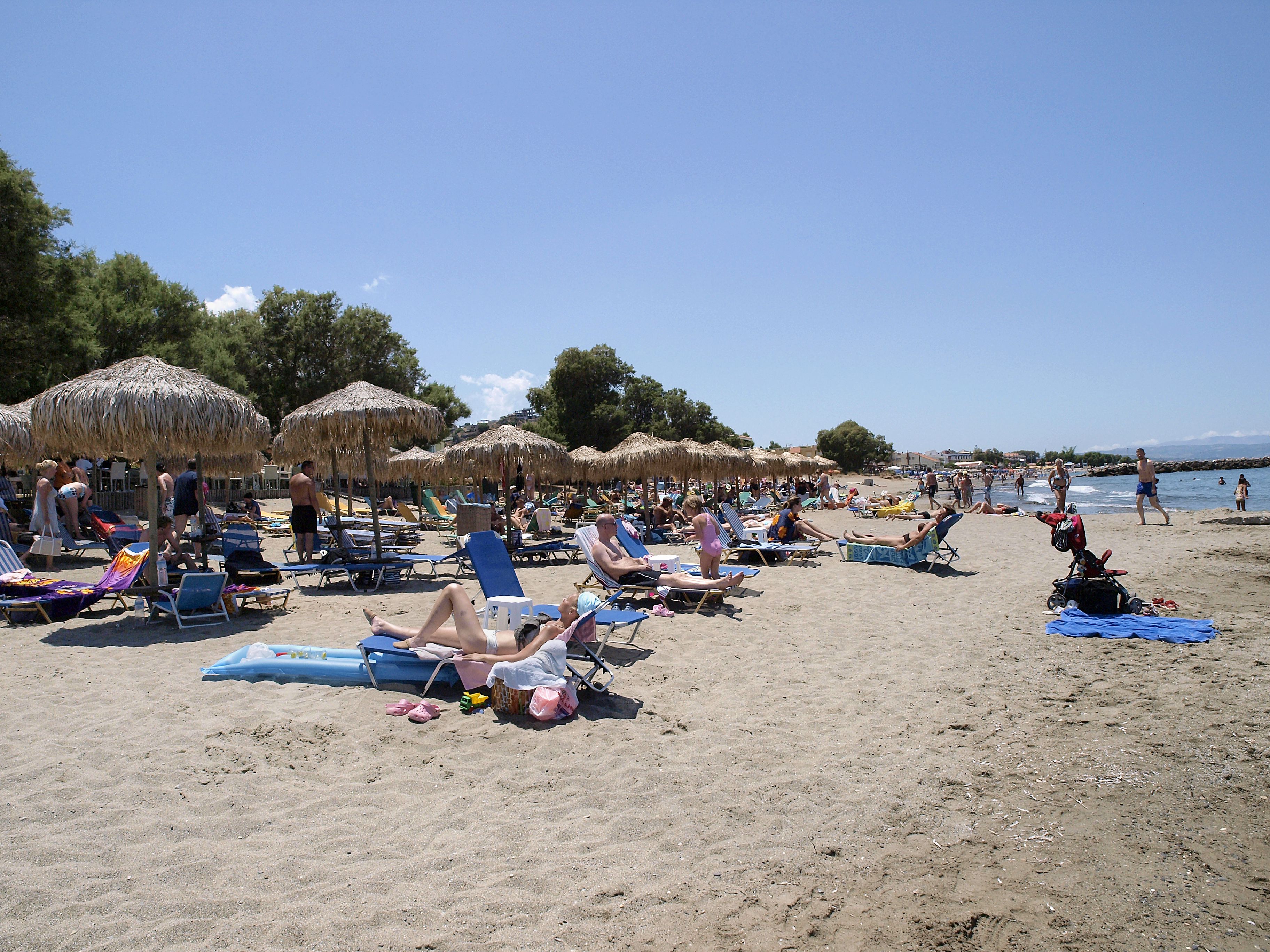 A beach with sun loungers and umbrellas, a clear sky, and a calm sea.