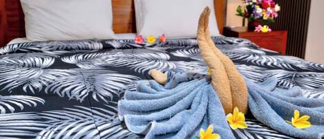 Una cama bien hecha con una colcha de estampado tropical, una toalla azul y un arreglo decorativo de toallas.