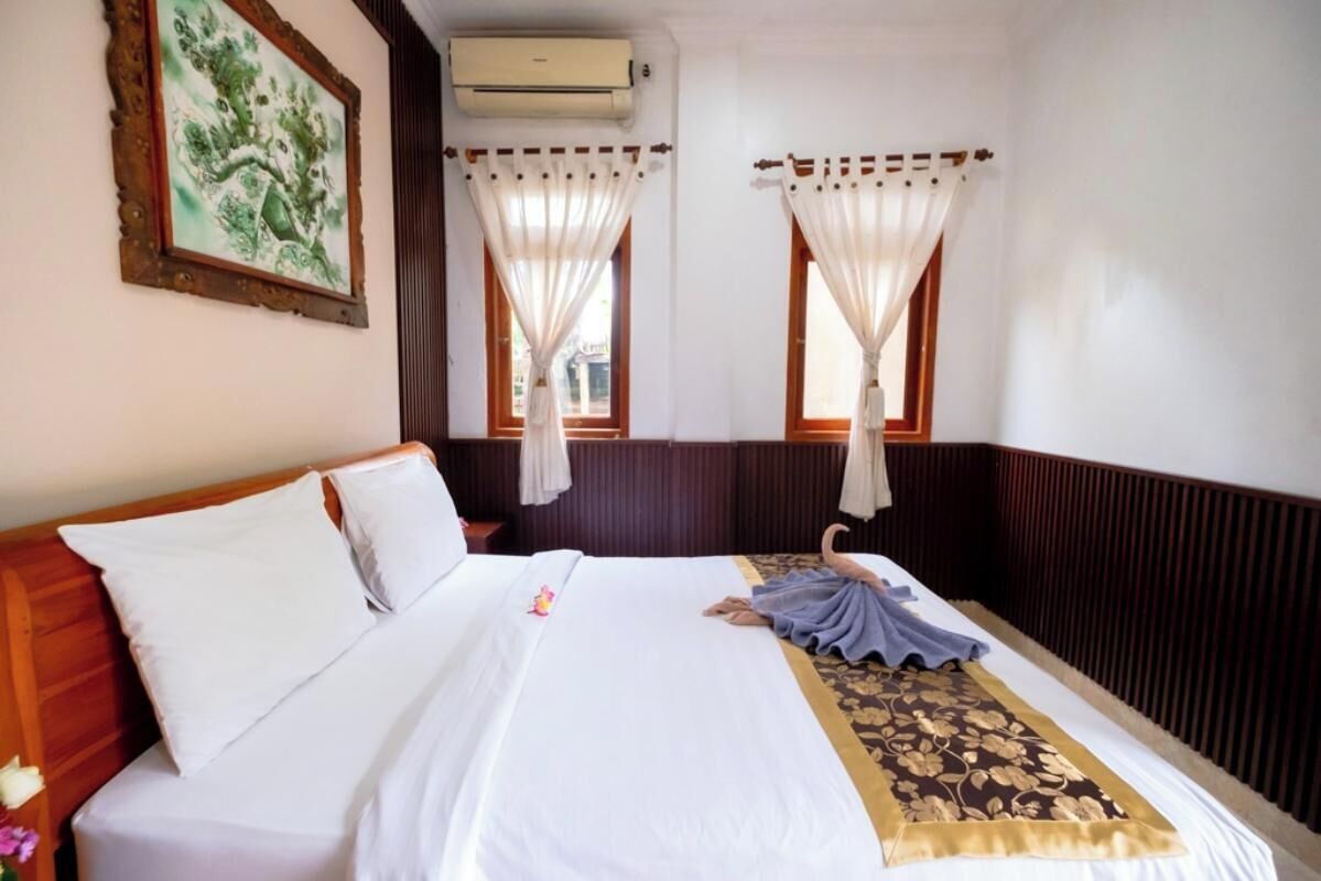 Une chambre d’hôtel avec un lit, des rideaux blancs, un tapis décoratif et un climatiseur fixé au mur.