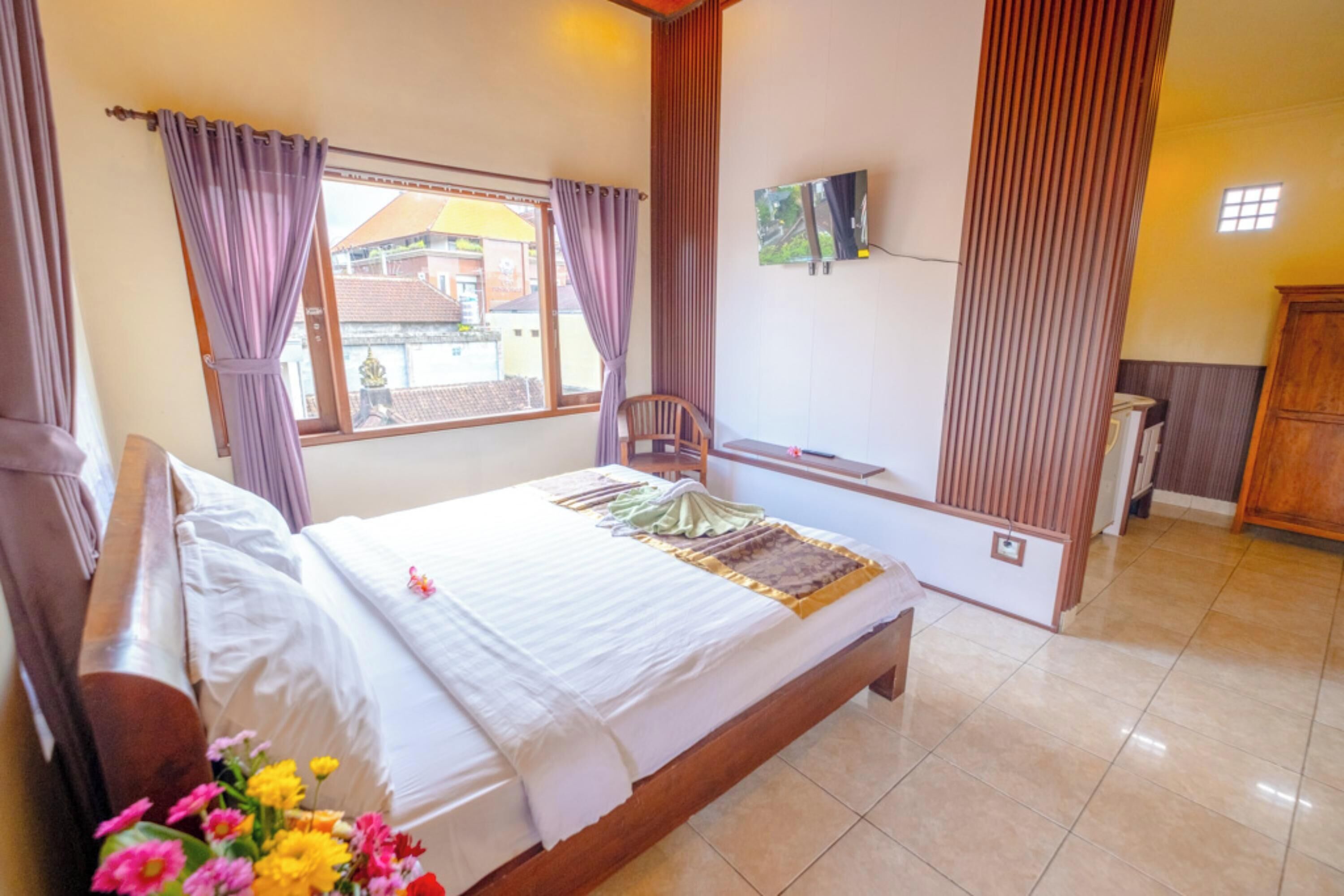 A bedroom with a bed, curtains, a TV mounted on the wall, and a wooden cabinet.