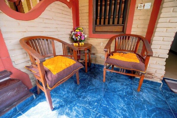 Dos sillas de madera con cojines amarillos, una mesita redonda con un centro de mesa floral y una ventana con barras verticales.