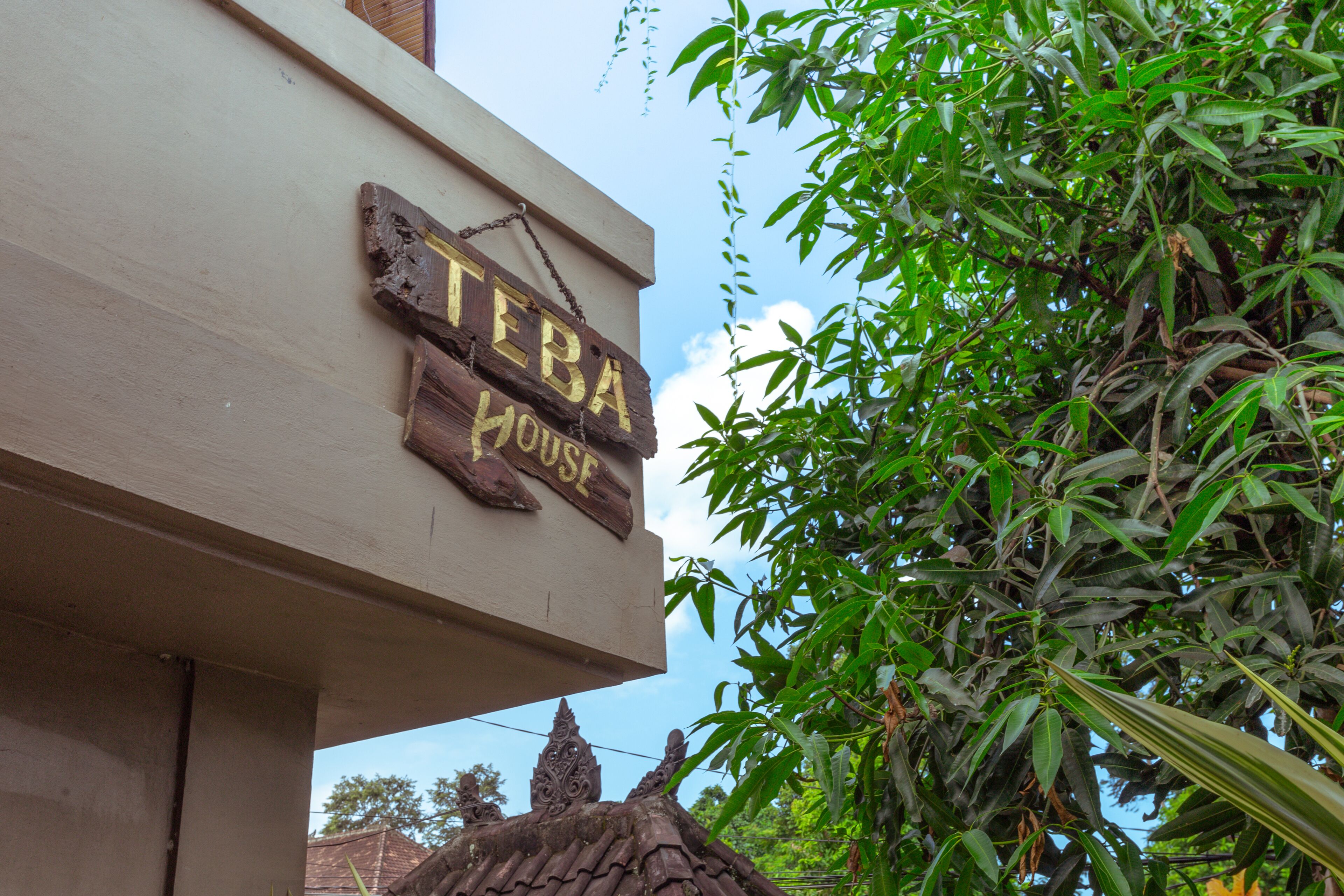 A wooden sign with the text "TEBA HOUSE" hanging from a building.