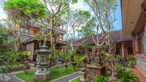 A courtyard with a stone pathway, potted plants, and traditional statues. - Teba House (Ubud)