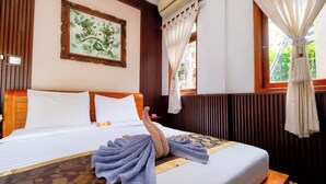 A hotel room with a neatly made bed, a framed artwork on the wall, and a window with curtains. - Teba House (Ubud)