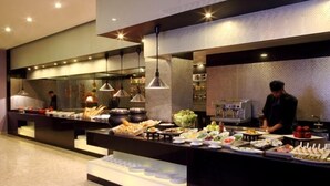A buffet setup with various food items and a person preparing food in the background. - Tuli Imperial (Nagpur)