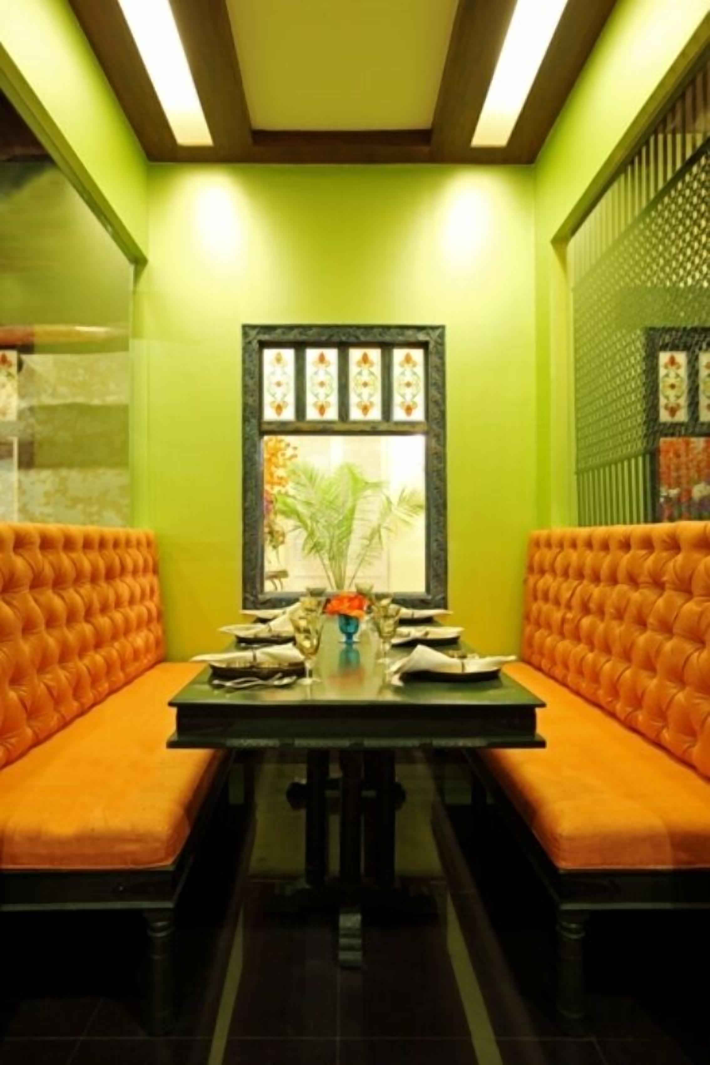 A dining area with a table set for two, surrounded by orange cushioned seating.