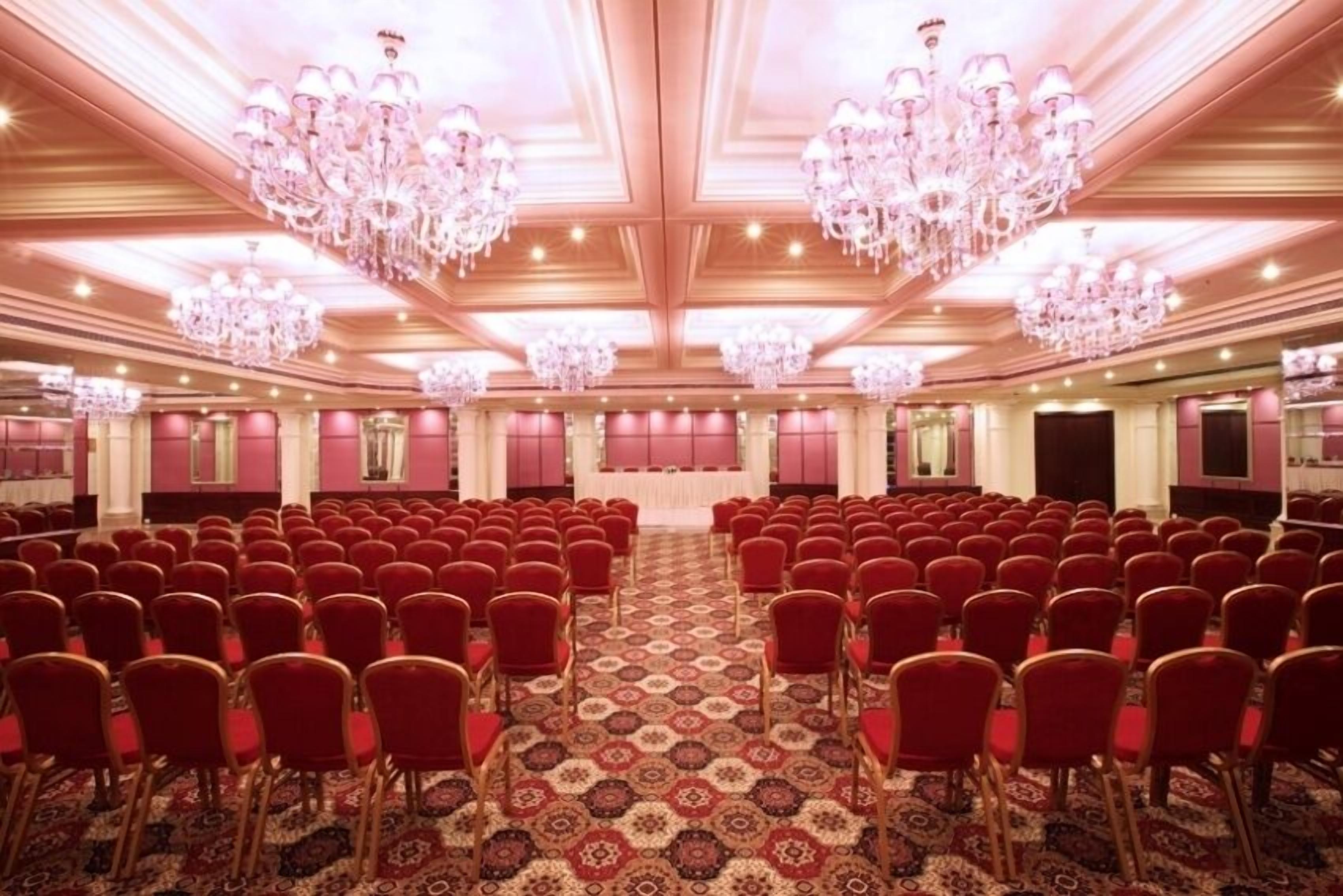 Une grande salle de conférence avec des rangées de chaises rouges, une moquette à motifs et des lustres décoratifs.