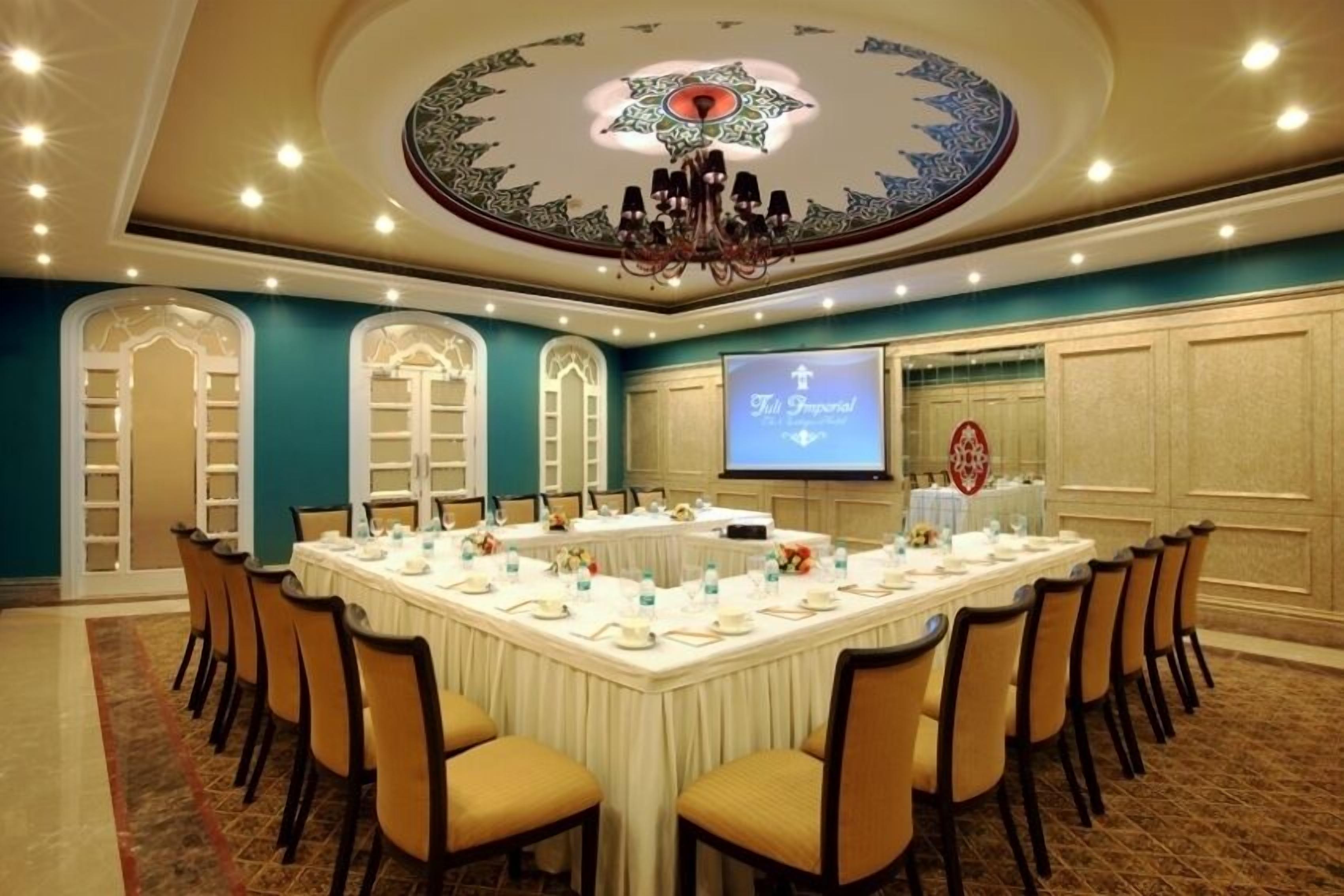 A conference room with a large oval table, chairs, a projector screen, and a chandelier.