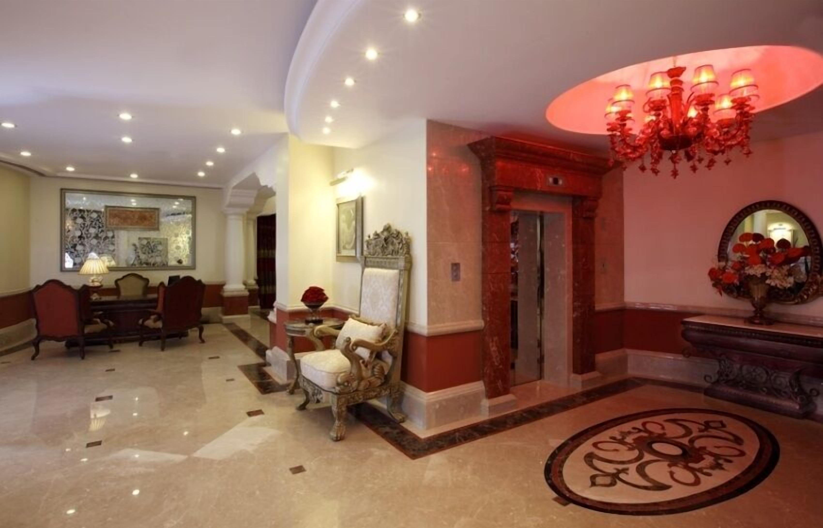 A lobby with a marble floor, a chandelier, a reception desk, and a dining area with chairs and a table.