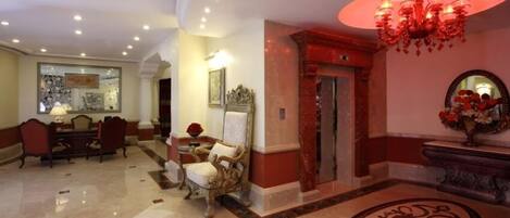 A lobby with a marble floor, a chandelier, a reception desk, and a dining area with chairs and a table.