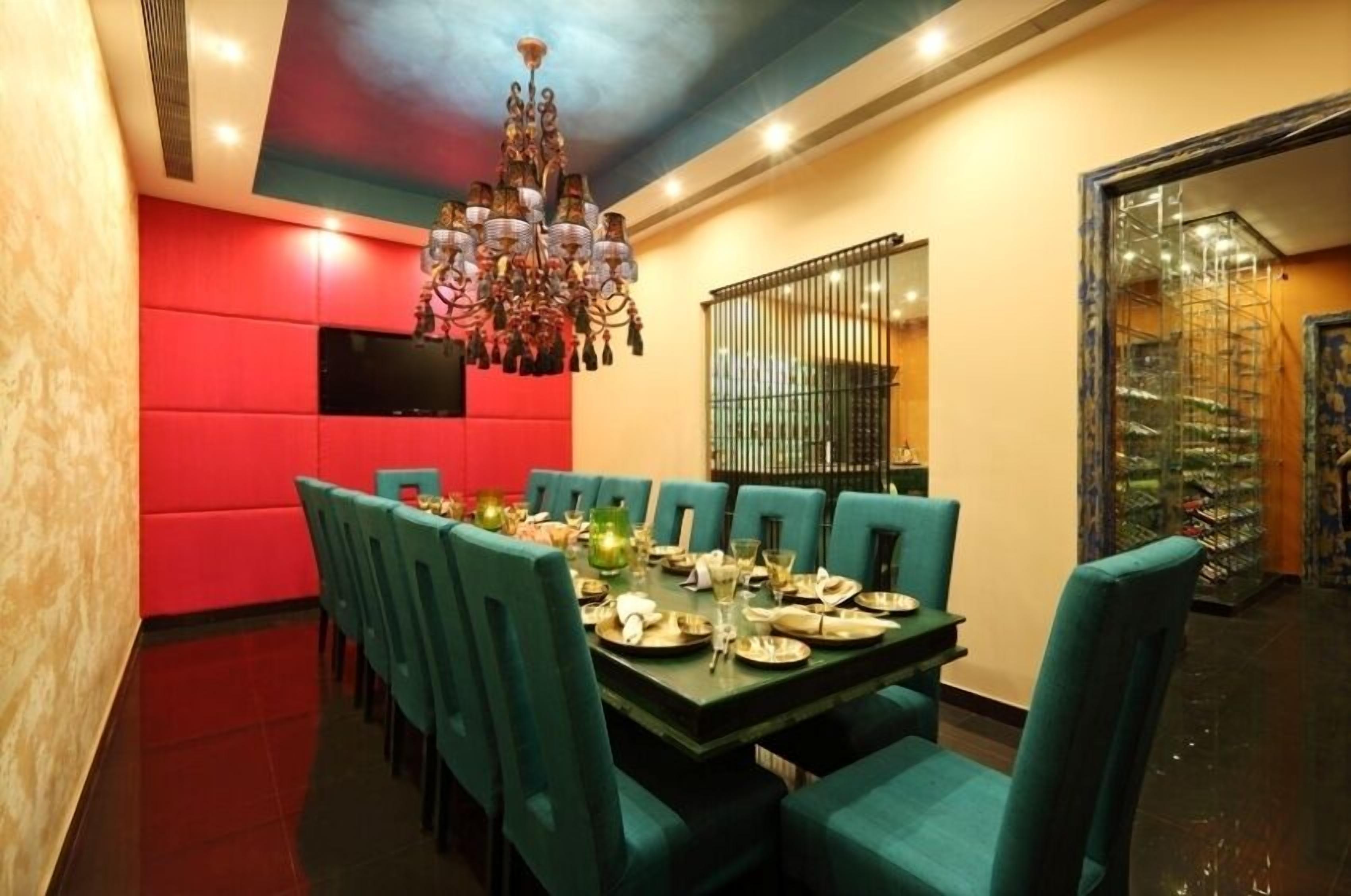 A dining area with a long table set for a meal, teal chairs, and a chandelier.