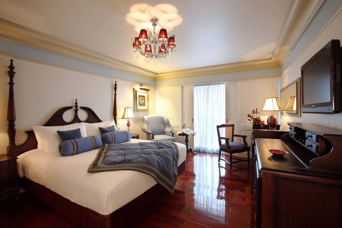 A hotel room with a large bed, a desk, a chair, a television, and a chandelier.