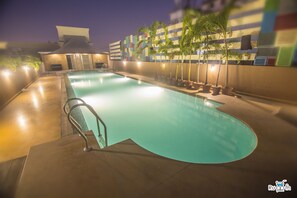 A swimming pool with a curved edge, surrounded by potted plants and a building with a modern design. - Tuli Imperial (Nagpur)