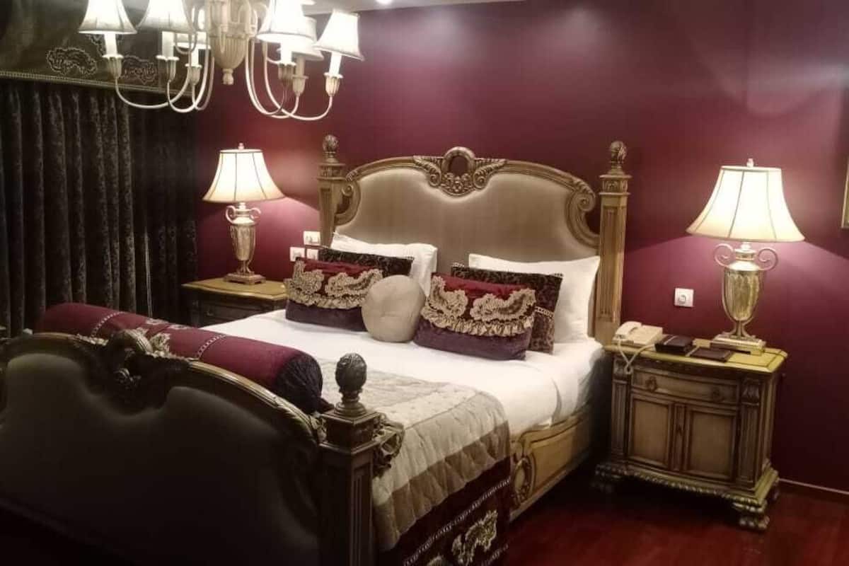 A bedroom with a large bed, ornate headboard, two bedside tables with lamps, and a framed picture on the wall.
