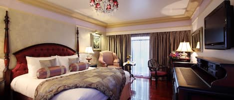A hotel room with a large bed, a desk, a chair, a television, and a chandelier.