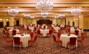 A banquet hall with round tables, red chairs, and chandeliers. - Tuli Imperial (Nagpur)