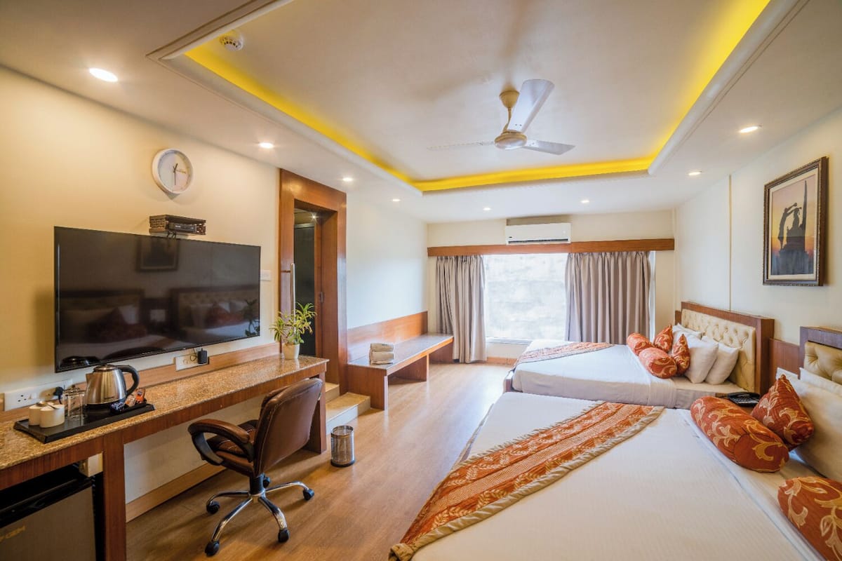 Een hotelkamer met een televisie, bureau, stoel, twee bedden, een raam en een airconditioning.