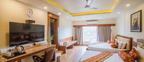 A hotel room with a TV, desk, chair, two beds, a window, and an air conditioning unit.