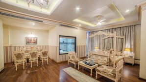 A room with a dining table, chairs, a sofa, a bed, and a window. - The Nagpur Ashok (Nagpur)