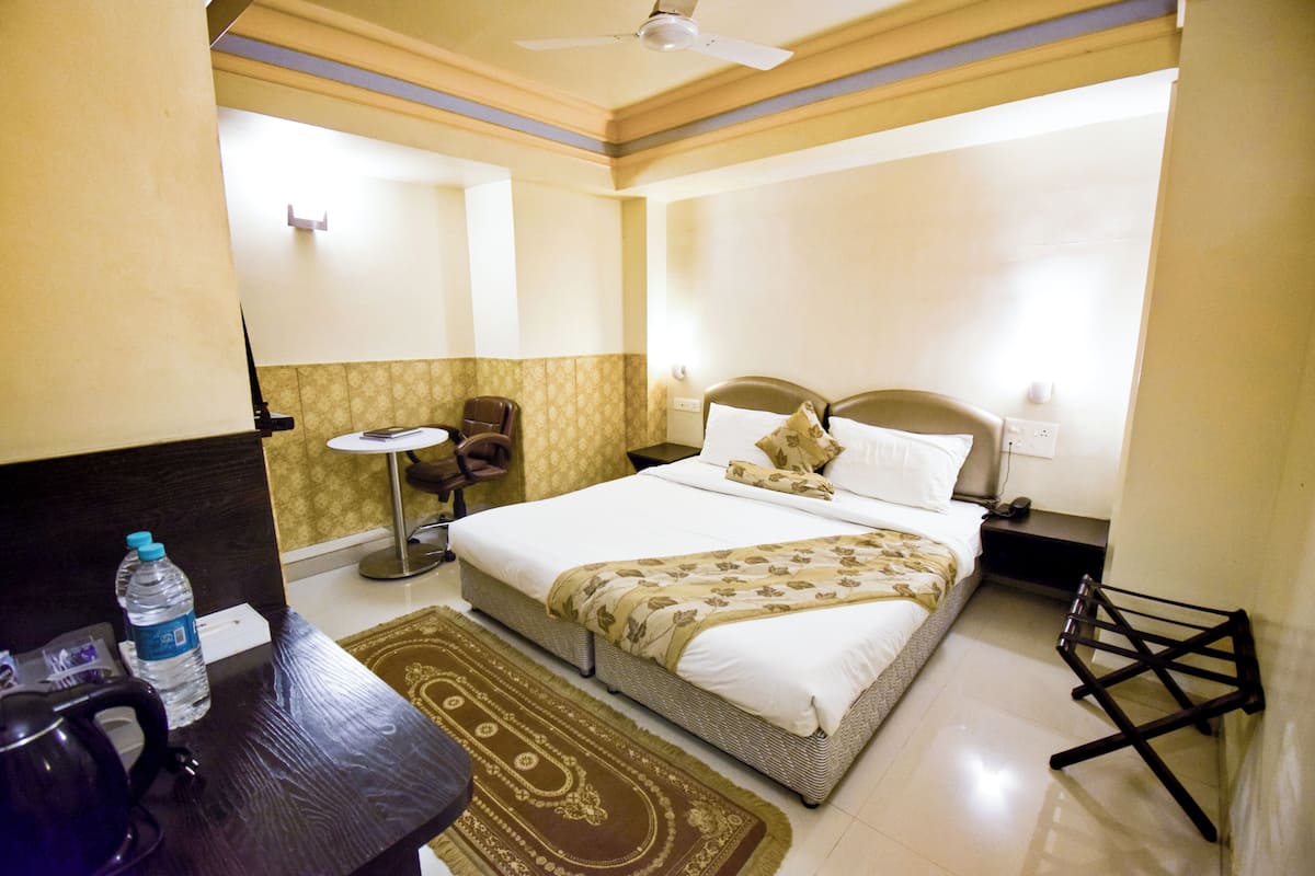 Een hotelkamer met een bed, een bureau, een stoel, een waterfles, een lamp en een plafondventilator.
