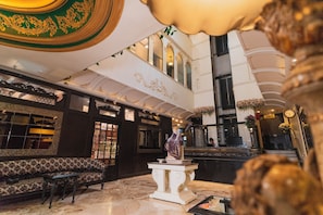 Un vaste hall d’entrée agrémenté de motifs décoratifs au plafond, d’une statue sur un piédestal et d’un espace détente avec des canapés à motifs.