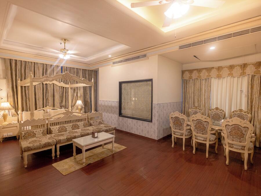 A spacious living room with a sofa set, a dining table with chairs, a large window, and a ceiling fan.