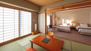 Une chambre d’hôtel traditionnelle japonaise avec un sol recouvert de tatamis, une petite table sur laquelle est posé un livre, deux lits, un bureau et un paravent coulissant de type shoji.