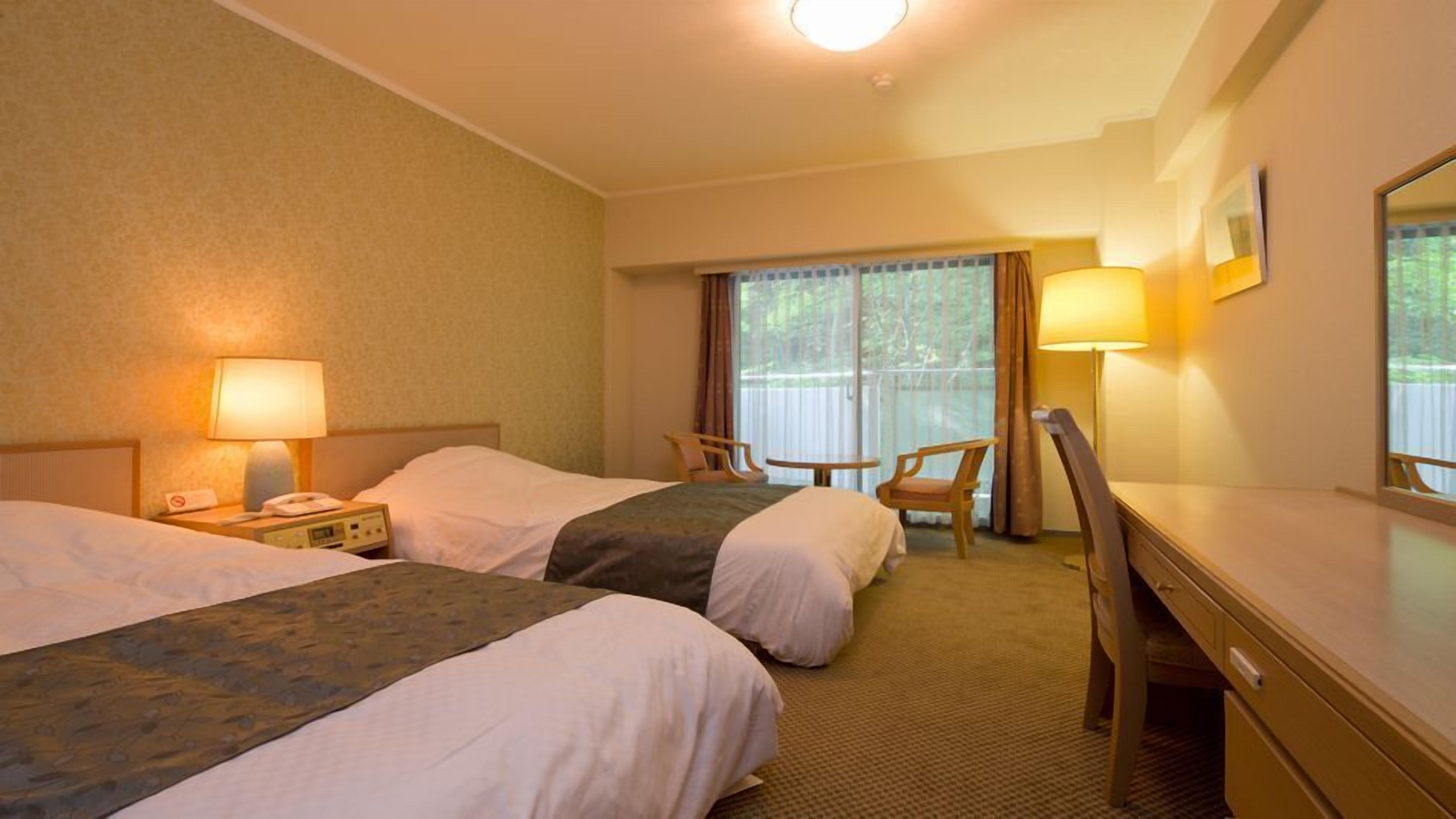 A hotel room with two beds, a desk, a chair, and a window with curtains.