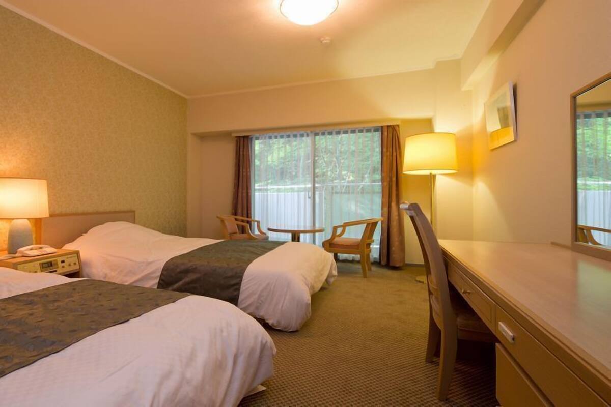 A hotel room with two beds, a desk, a chair, and a window with curtains.