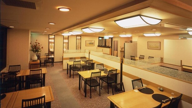A restaurant with multiple dining tables and chairs, a counter, and a wall-mounted television. - Merveille Arima (Kobe)