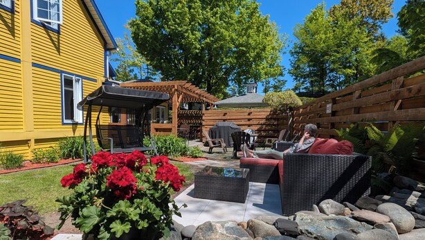 Un patio con mobiliario exterior, una pérgola y un edificio amarillo al fondo.