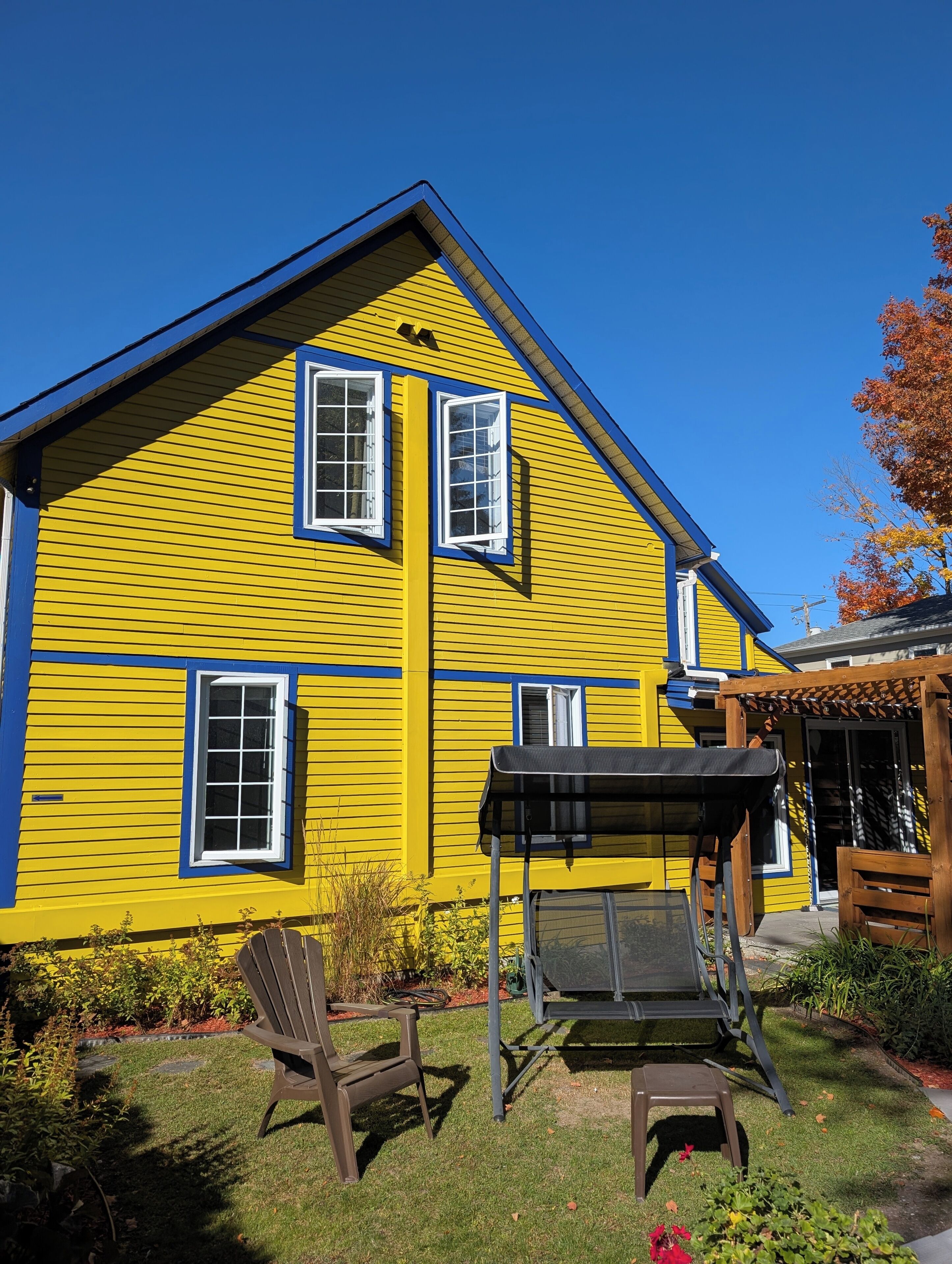Una casa gialla con tetto blu, due finestre e un patio con tavolo e sedie.