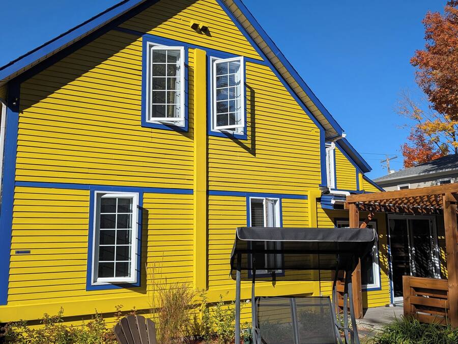 Una casa gialla con tetto blu, due finestre e un patio con tavolo e sedie.
