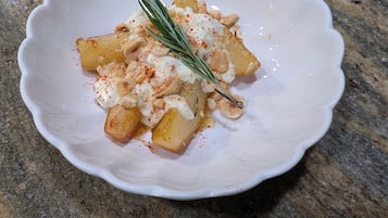 A white bowl with a scalloped edge containing a dish of food, possibly potatoes, with a sprig of rosemary and a sprinkle of red seasoning on a granite countertop.