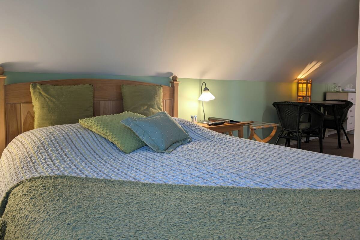 A bedroom with a bed, pillows, a nightstand, a lamp, a chair, and a small table.