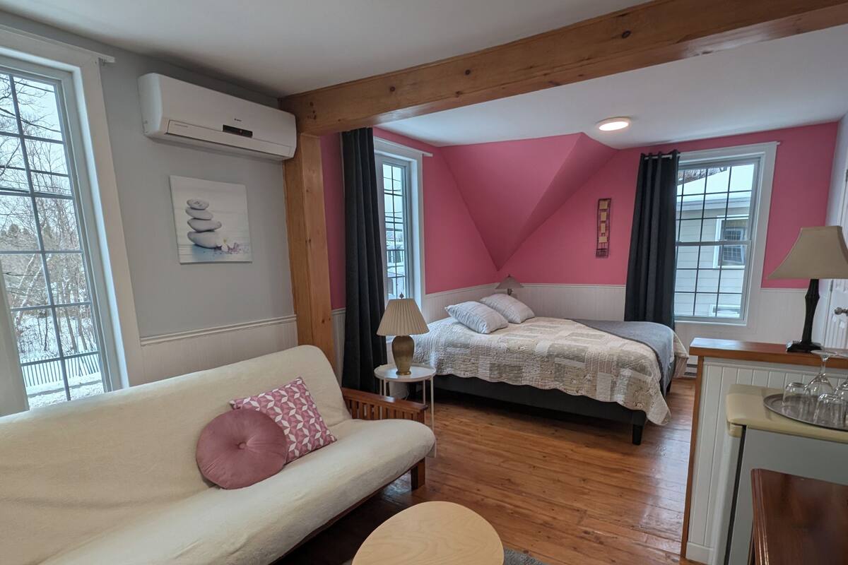 A bedroom with a bed, a sofa, a small table, and a window.