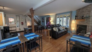 Un salón espacioso con chimenea, una zona de comedor con manteles a rayas y una escalera que sube a otro nivel.