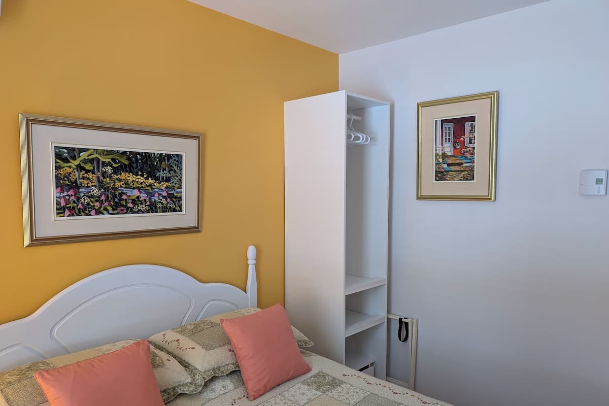 A bedroom with a bed, a wardrobe, and two framed pictures on the wall.