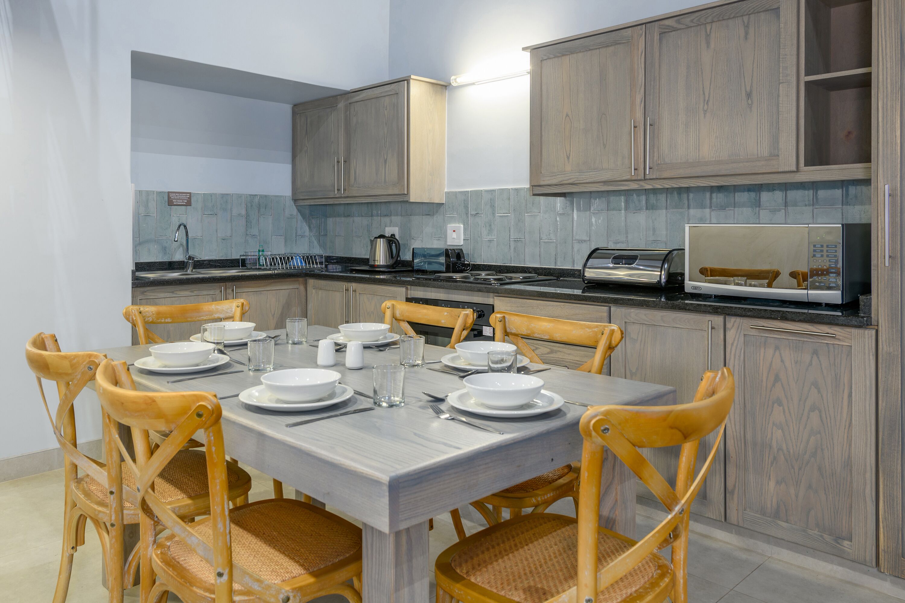 A modern kitchen with wooden cabinets, a grey countertop, and a dining table set for four.