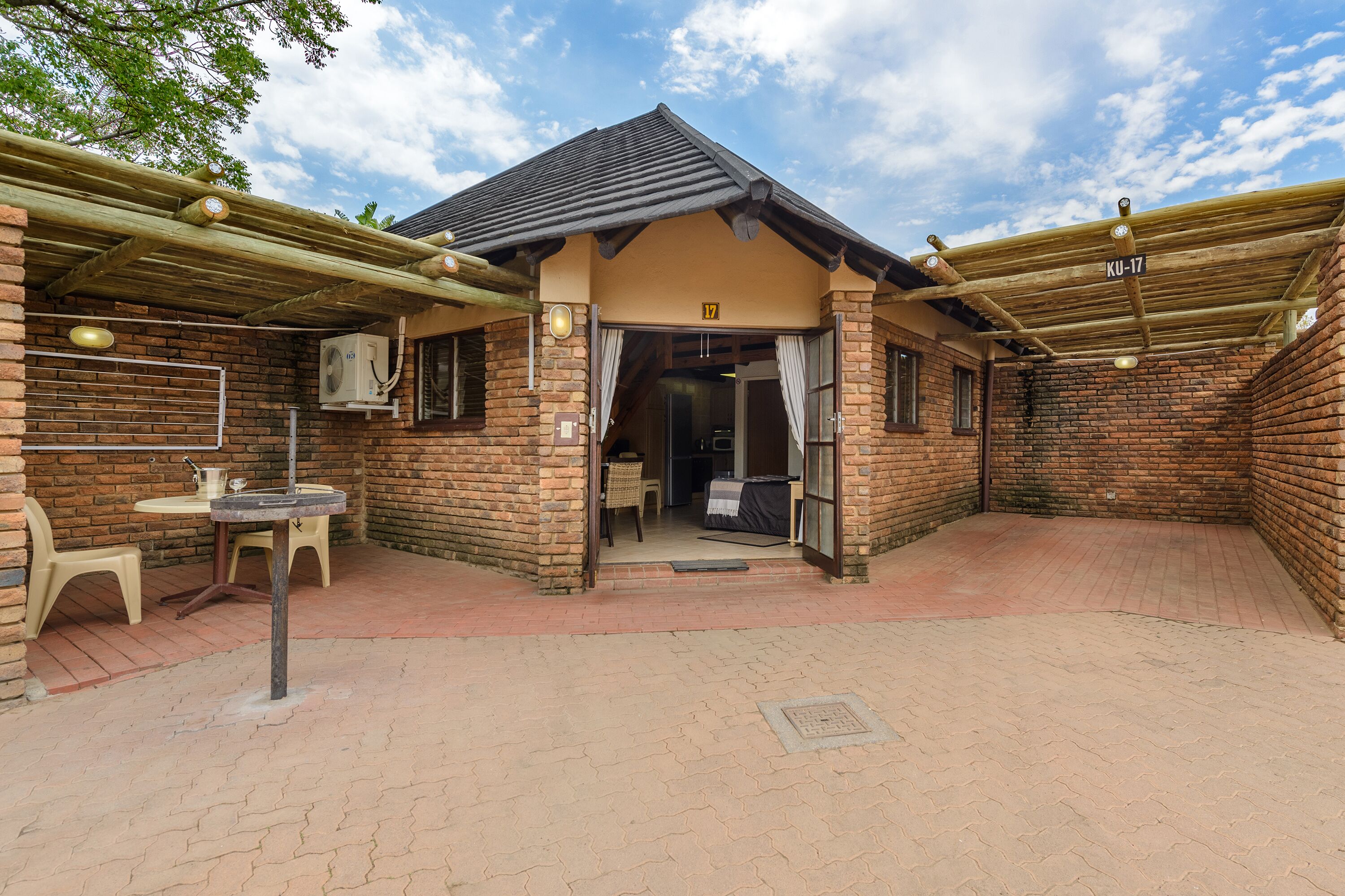 A brick building with a covered patio area, a table with chairs, and an air conditioning unit.