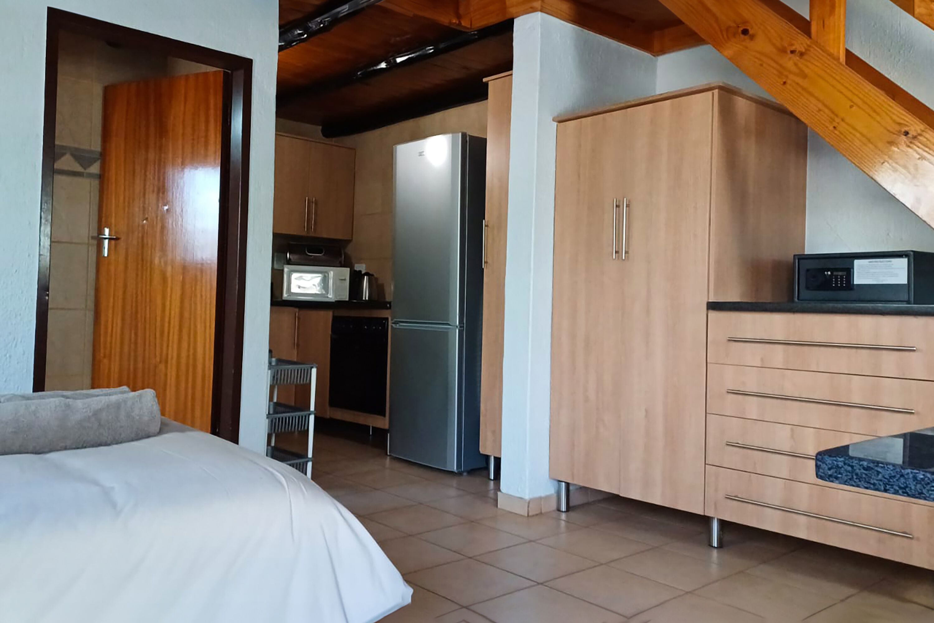 Une chambre d’hôtel compacte comprenant un coin cuisine, un lit et une poutre en bois au plafond.