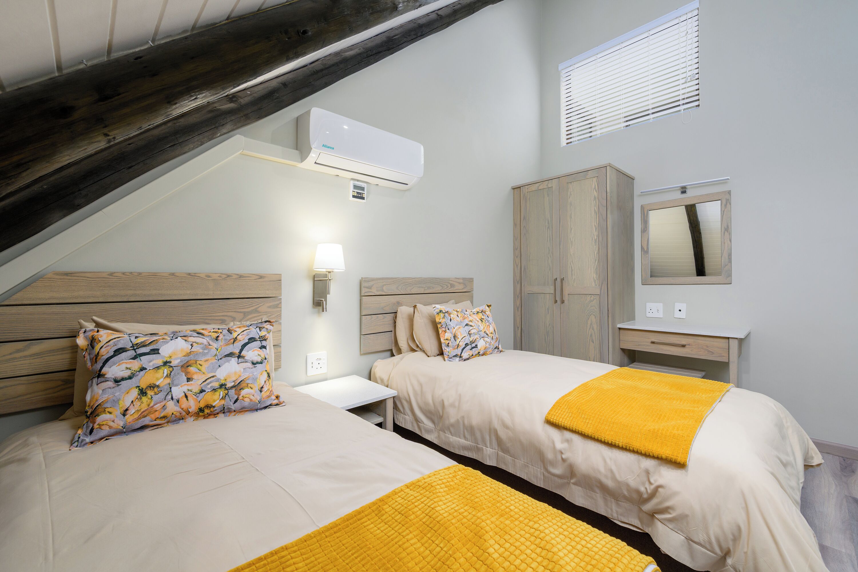 Un dormitorio con dos camas, cabecero de madera, mesita de noche, lámpara, armario y aire acondicionado.