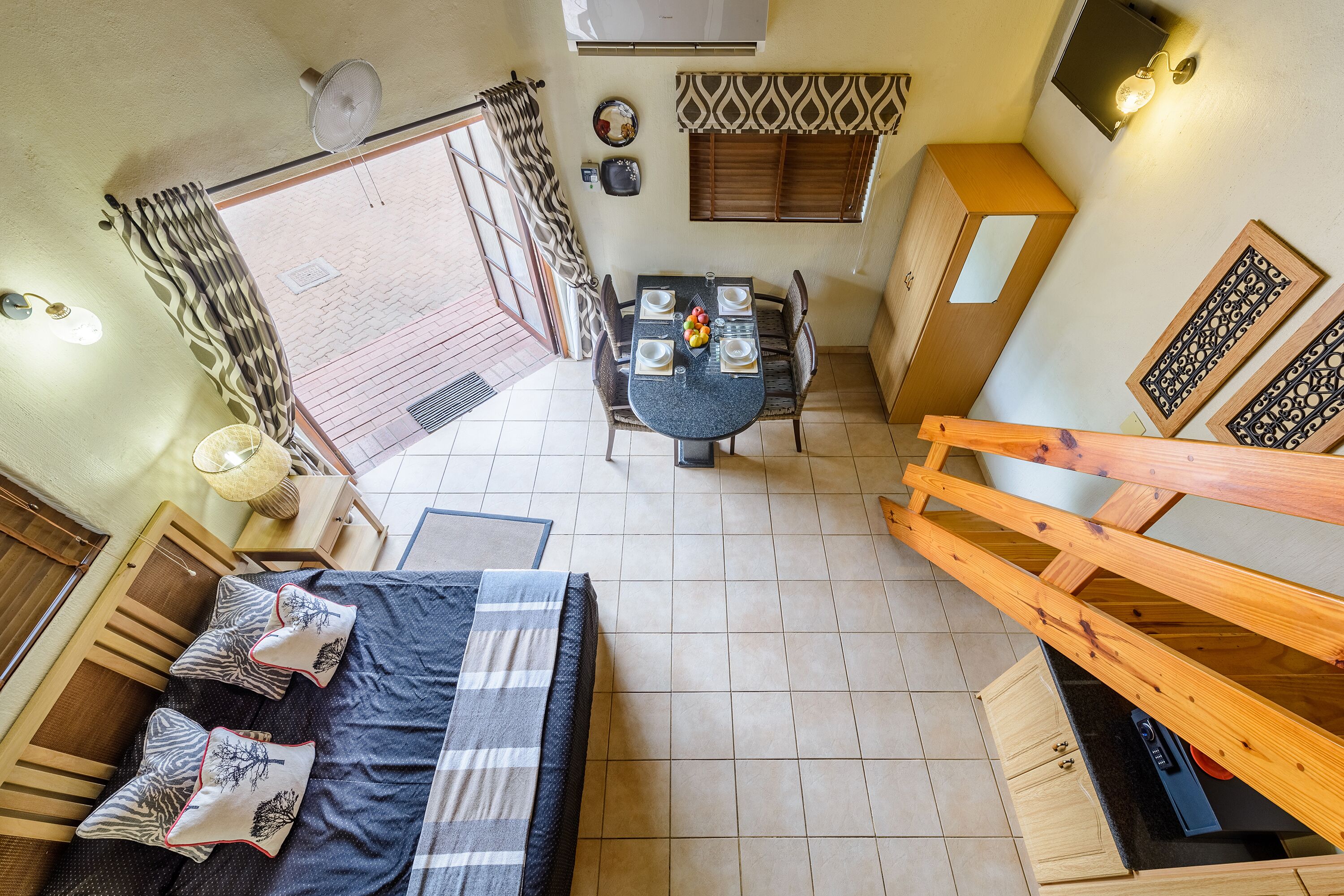Une pièce de taille modeste comprenant un lit, une table à manger avec des chaises, un escalier en bois et un petit coin cuisine.