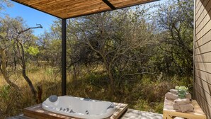 Une terrasse en bois avec un jacuzzi, une table en bois avec des serviettes et une vue sur un paysage naturel.